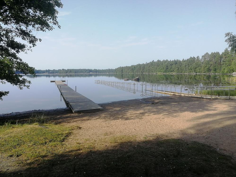 Sandstrand med två bryggor. En i trä och en i metall med räcken på båda sidorna 