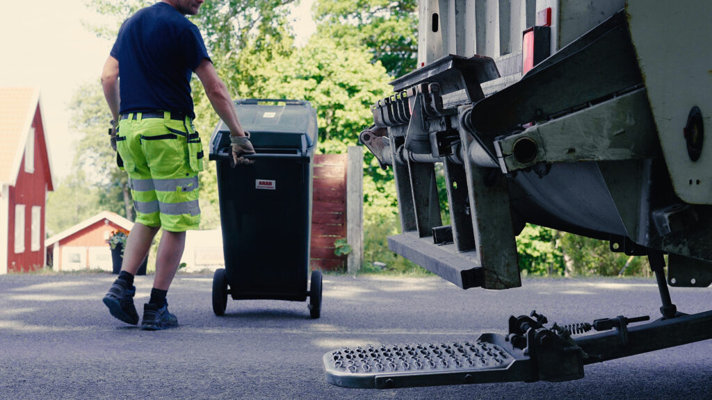 Person kör ett sopkärl mot bakdelen till en sopbil.