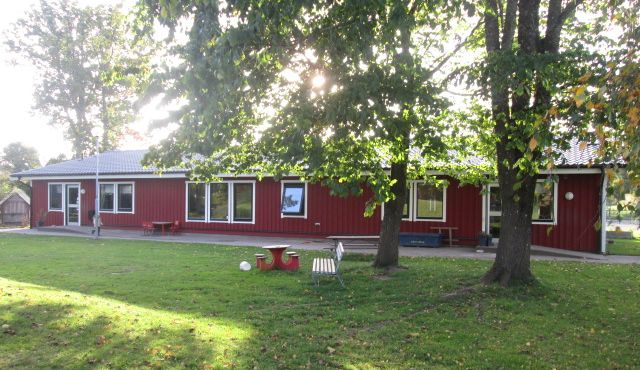 Röd förskolebyggnad med gräsmatta och träd på gården.