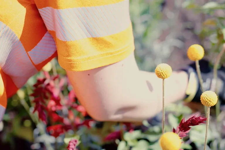 Varselklädd person som rensar ogräs i en rabatt med gula och röda blommor.