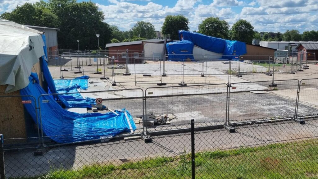 Översiktsbild över skolområdet med byggstaket omringar de delar av skolan som är bortröjda efter branden. Blå presenning hänger vid anslutande skolbyggnader.