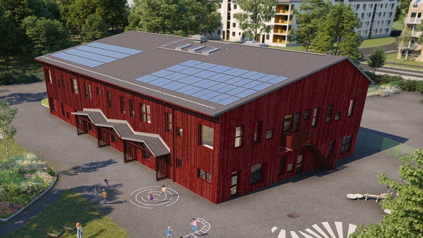 Röd byggnad med träfasad, solceller på taket samt ett par ingångar. Utemiljö med asfalt och grönytor.