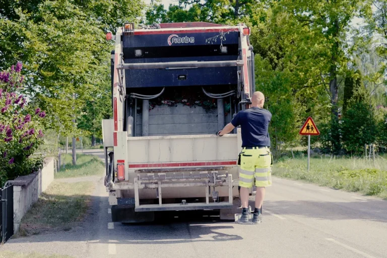En man som står bredvid en sopbil på en väg.