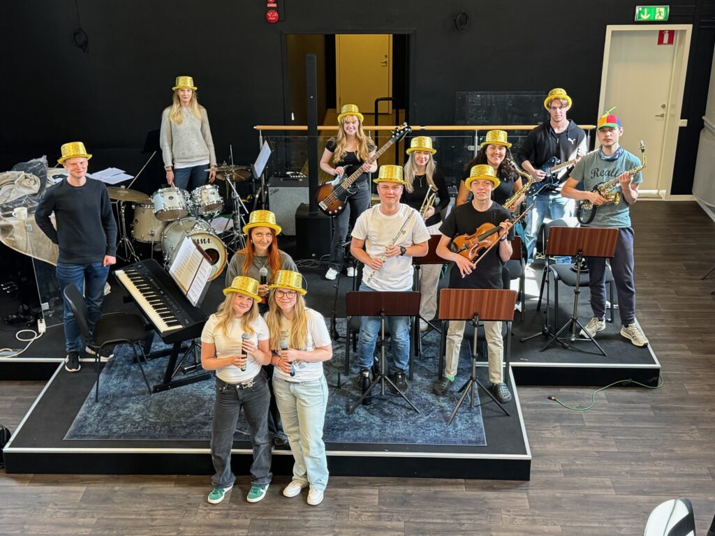 En grupp ungdomar med guldhattar som står på en scen med olika instrument.