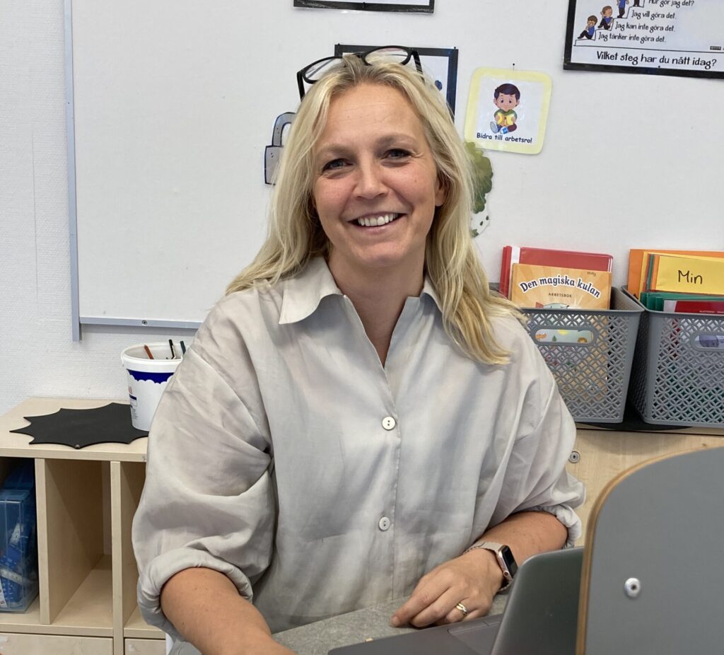 en blond kvinna sitter bakom ett skrivbord och ser glad ut