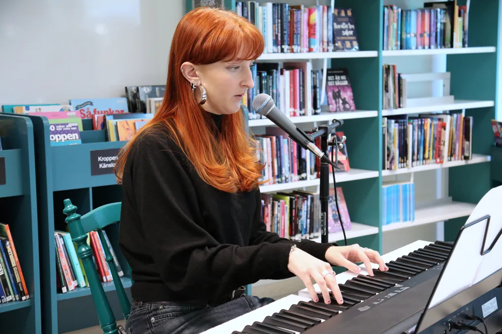 En kvinna sitter vid ett piano framför en mikrofon.