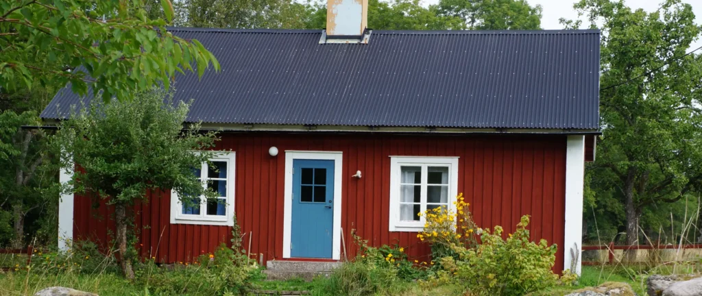 Ett rött hus med en blå dörr omgivet av stenar.
