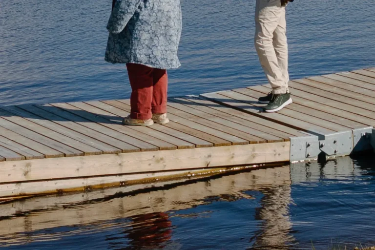 Två personer som står på en brygga nära ett vattendrag.