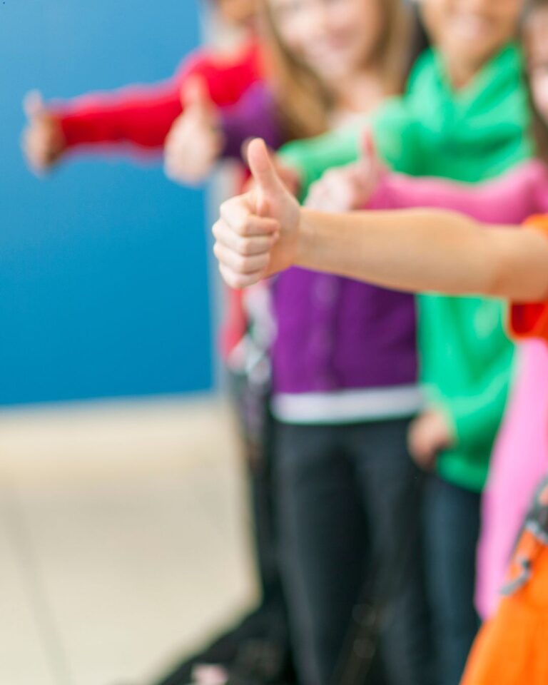 Barn i oskärpa står med färgglada kläder och en ger tummen upp.