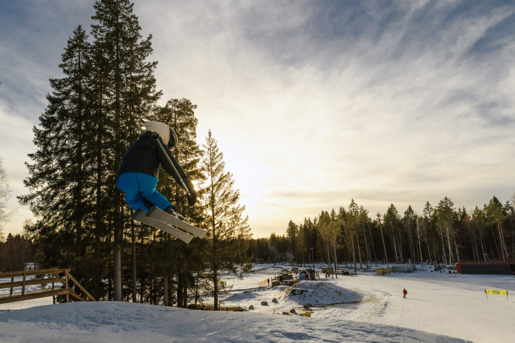 Barn hoppar med snowboarden i skidbacken med vintersolen framför sig.