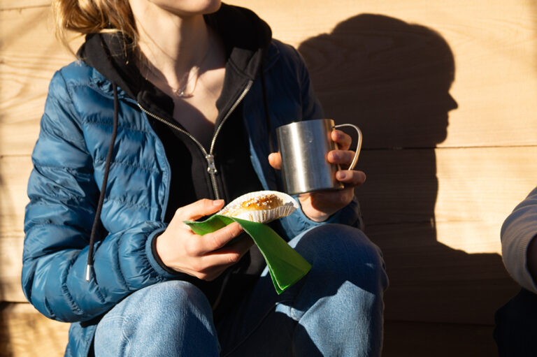 kvinna fikar med bulle och kaffe ute i naturen.