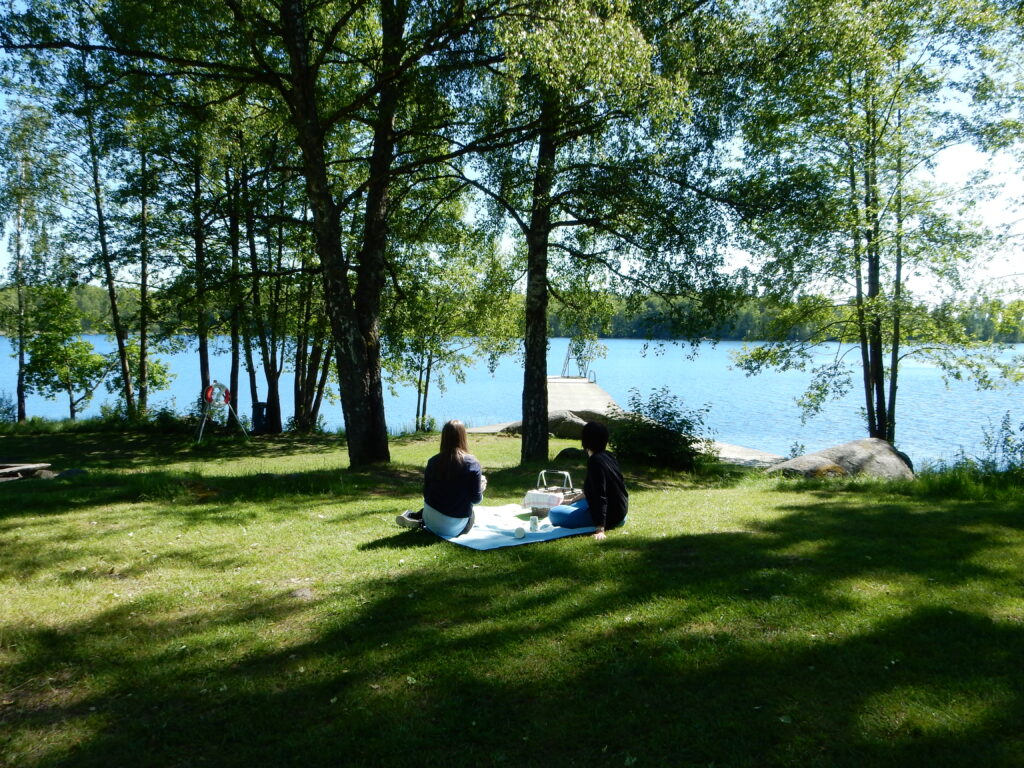 Två personer har picknick på grönyta framför en badplats.