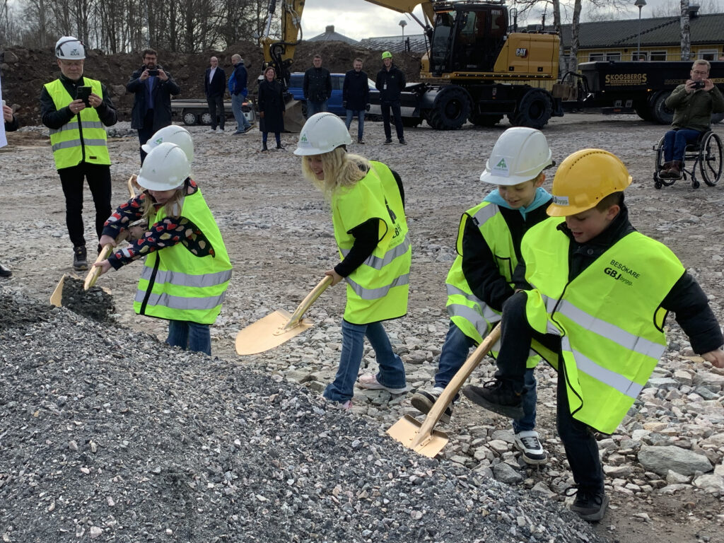 En grupp barn med spadar, bygghjälmar och gula varselvästar.