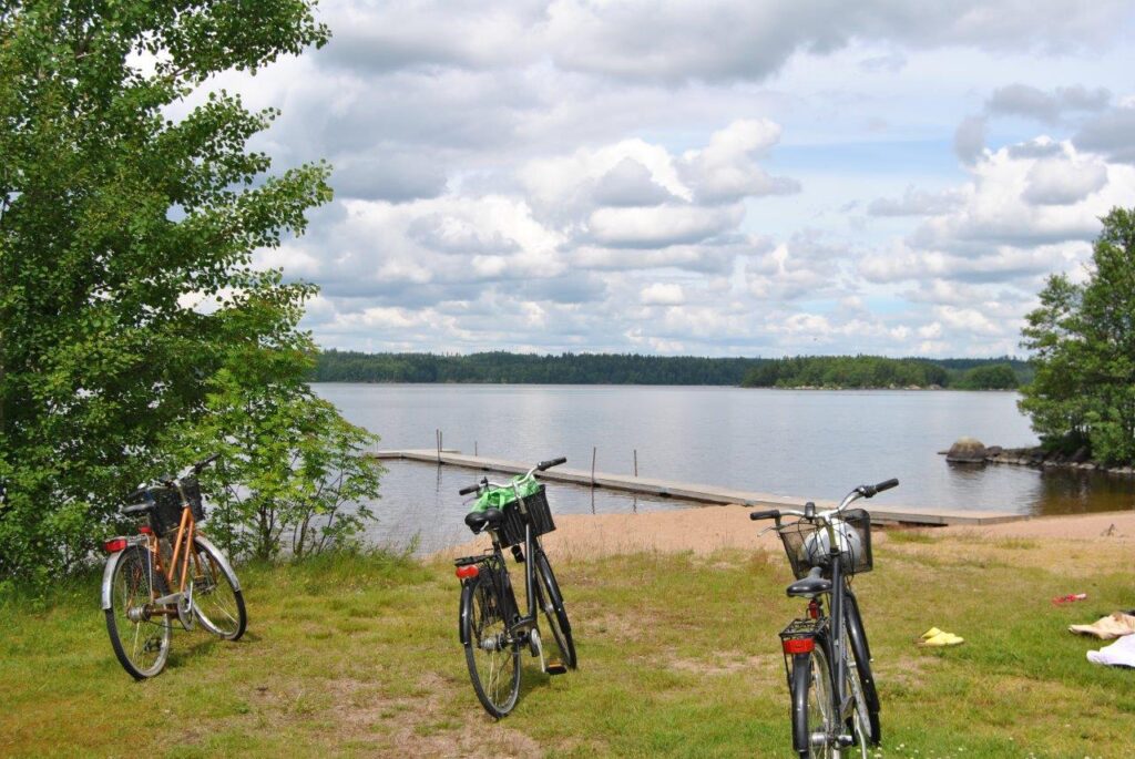 Tre cyklar med handdukar i cykelkorgarna står parkerade på en gräsyta vid en badplats.