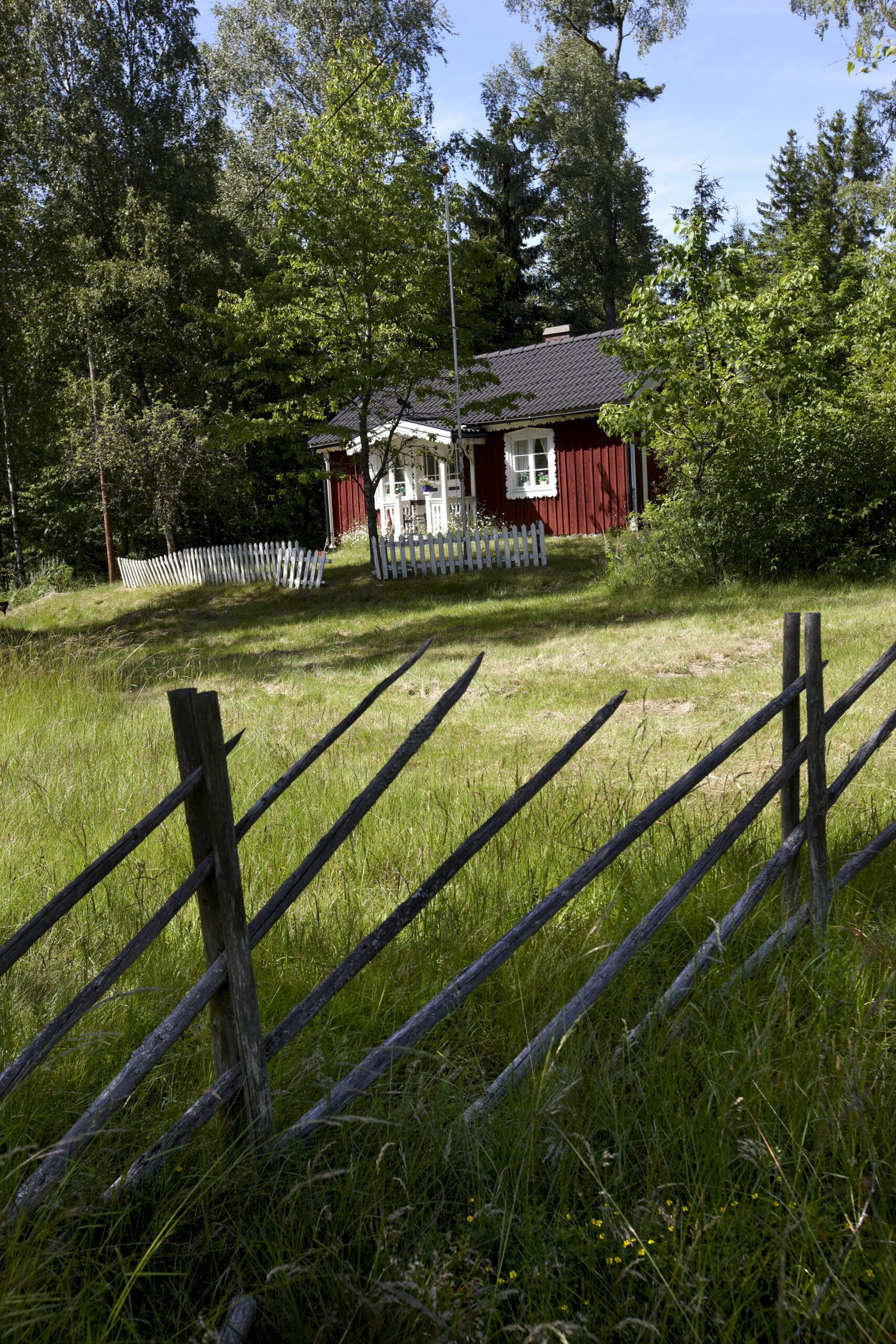 Ett rött hus i skogen bakom ett staket.