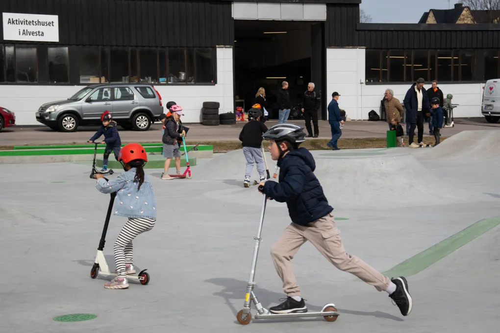 En ung pojke på en sparkcykel bredvid en liten flicka på en sparkcykel.