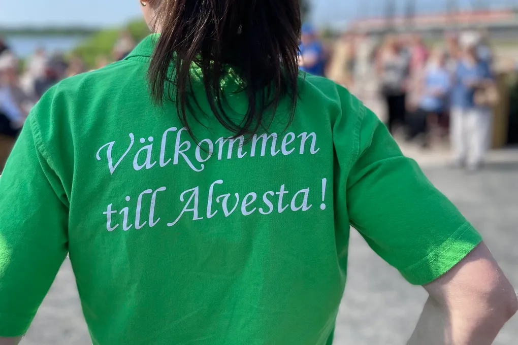 En kvinna i grön tröja som det står Välkommen till Alvesta på