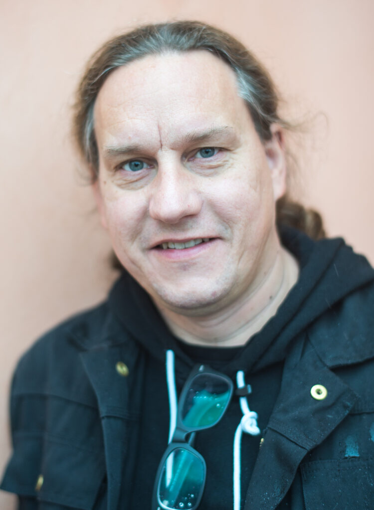 Ett porträtt på en medelålders man med uppsatt hår och svarta kläder.