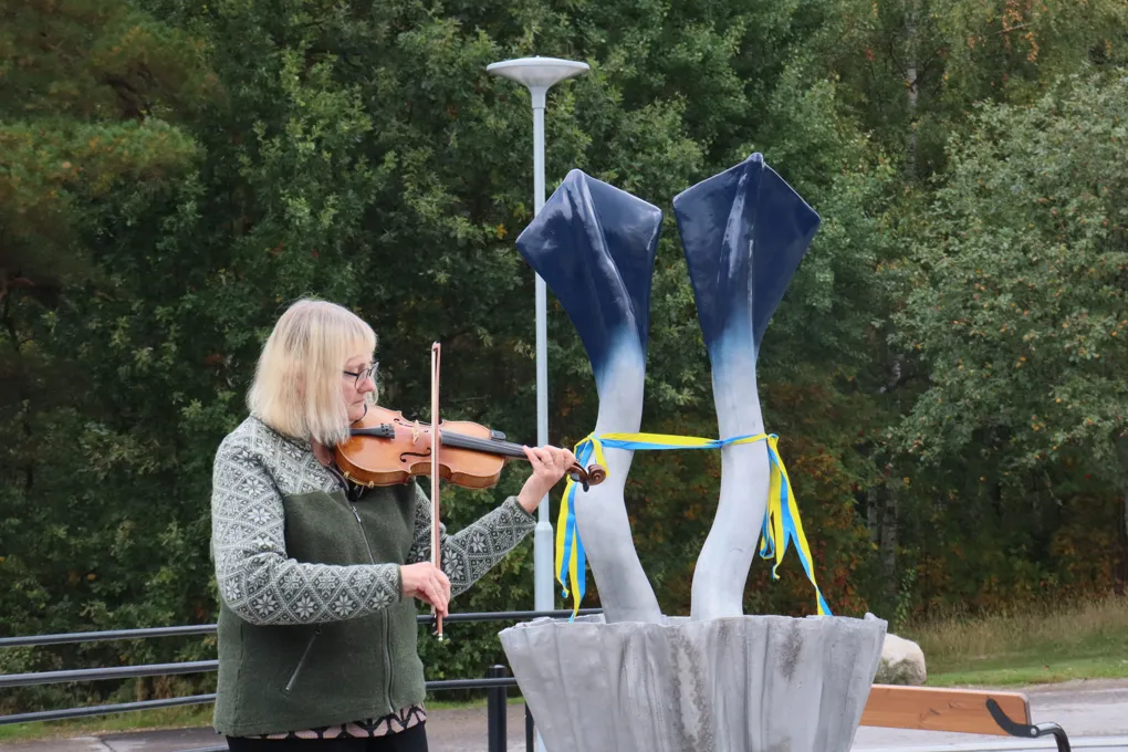 En kvinna som spelar fiol framför en skulptur.